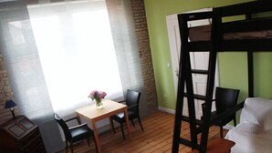 Ein Zimmer mit einem Etagenbett, einem Holztisch mit Stühlen, einem kleinen Schreibtisch und einem Fenster mit Vorhängen.