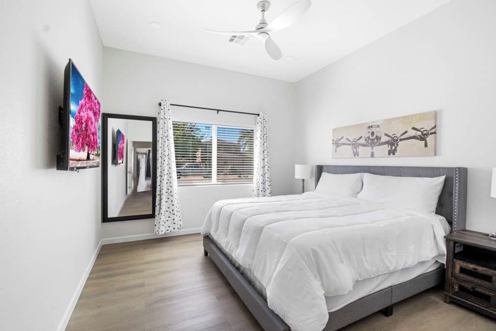 A bedroom with a bed, a ceiling fan, a window with blinds, and a painting on the wall.