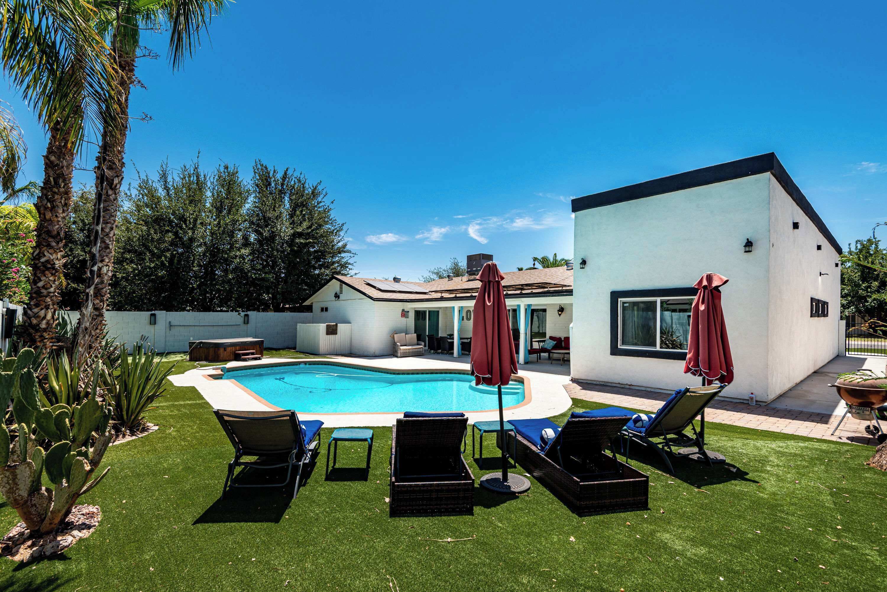 A swimming pool with lounge chairs and umbrellas, surrounded by a well-maintained lawn and palm trees.