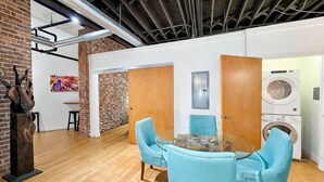 A modern interior with a round glass table, light blue chairs, a brick wall, a painting, and a washing machine. - Downtown Music City Loft living! ~Steps to the Ryman and Broadway (Nashville)