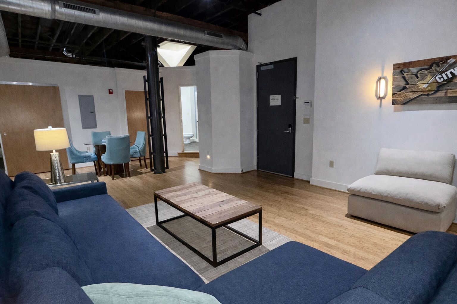 Een moderne woonkamer met blauwe banken, een houten salontafel en een eethoek met stoelen en een lamp.