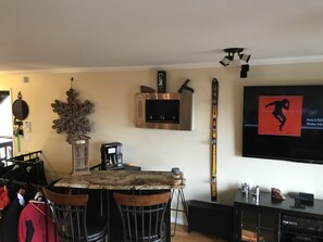 Una sala de estar con comedor, televisor montado y un esquí en la pared.