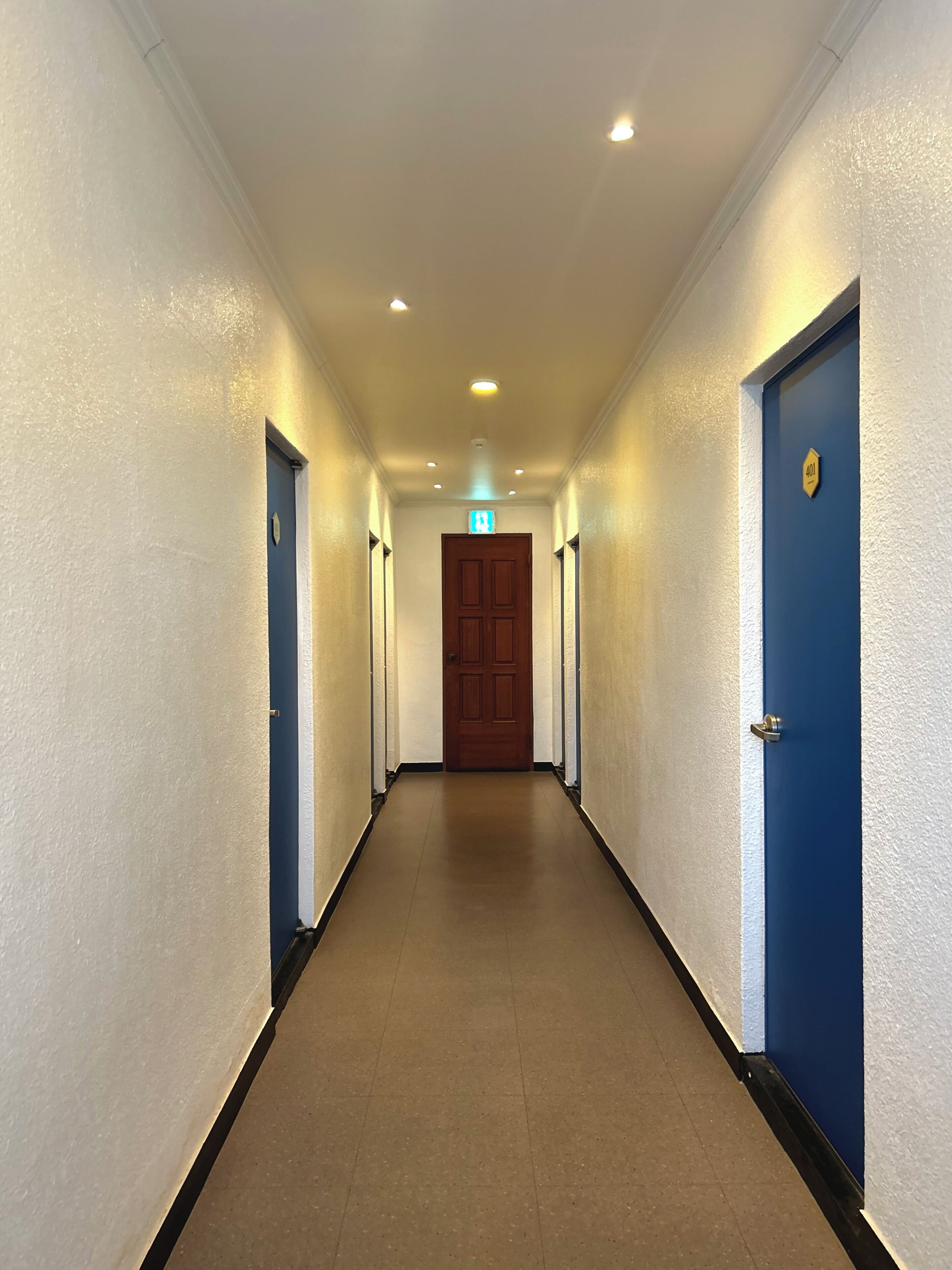A hallway with white walls, a brown floor, and blue doors.