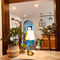 A well-lit hallway with a marble floor, potted plants, a lamp, and framed certificates on the wall.