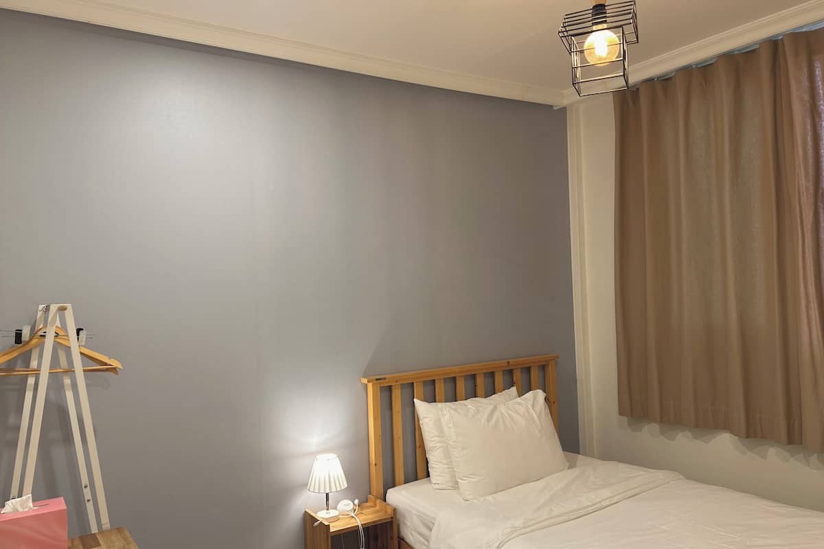 A bedroom with a wooden bed, a bedside table with a lamp, a wooden hanger, and a pink tissue box.