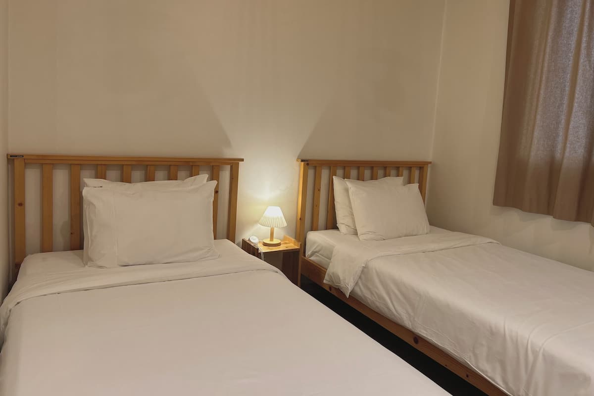 A hotel room with two single beds, a nightstand with a lamp, and a window with curtains.