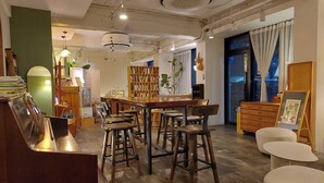 Un café chaleureux avec un bar en bois, des tabourets hauts, une bibliothèque et une grande fenêtre avec des rideaux.