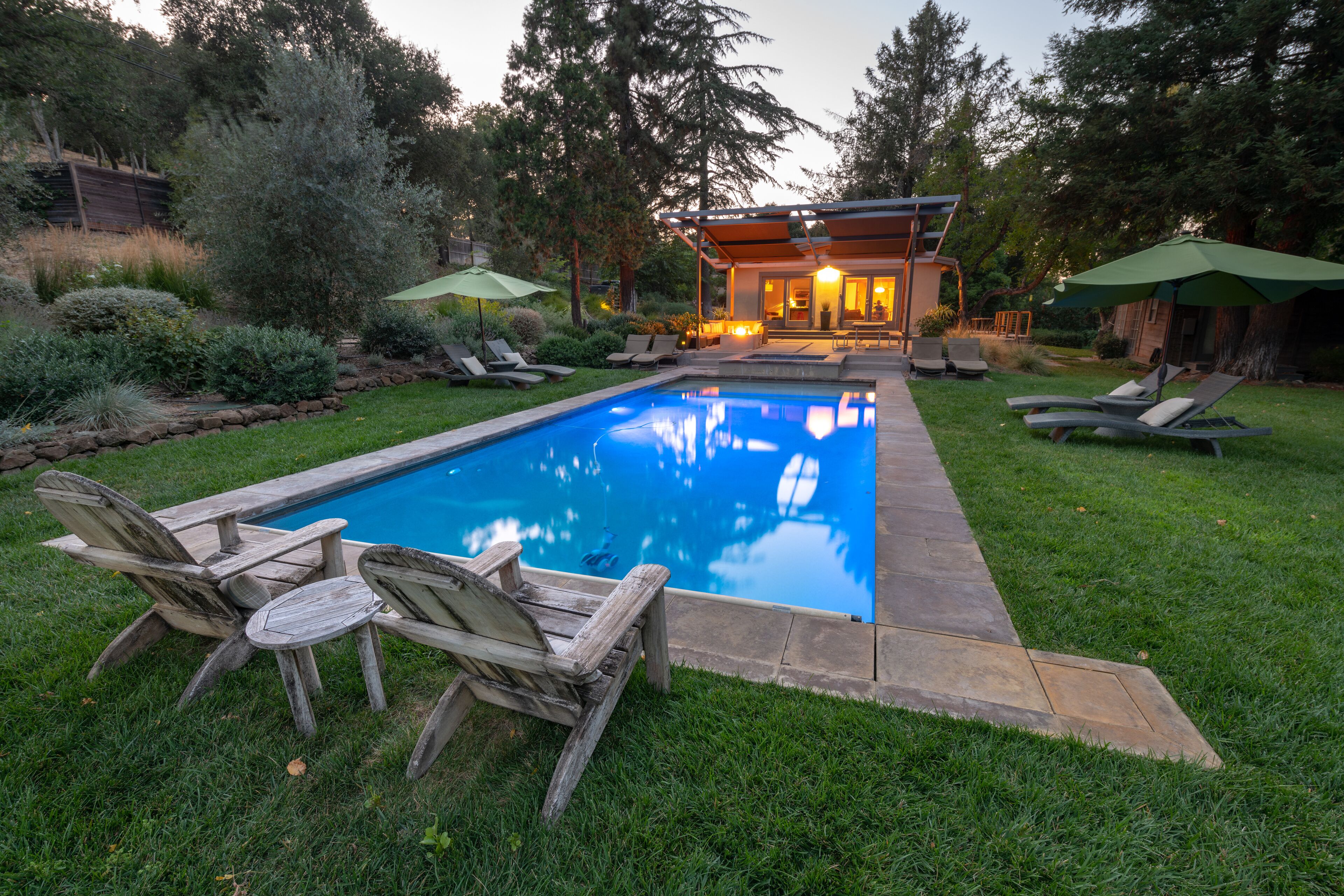 A swimming pool with lounge chairs and umbrellas, surrounded by a well-maintained lawn and trees.