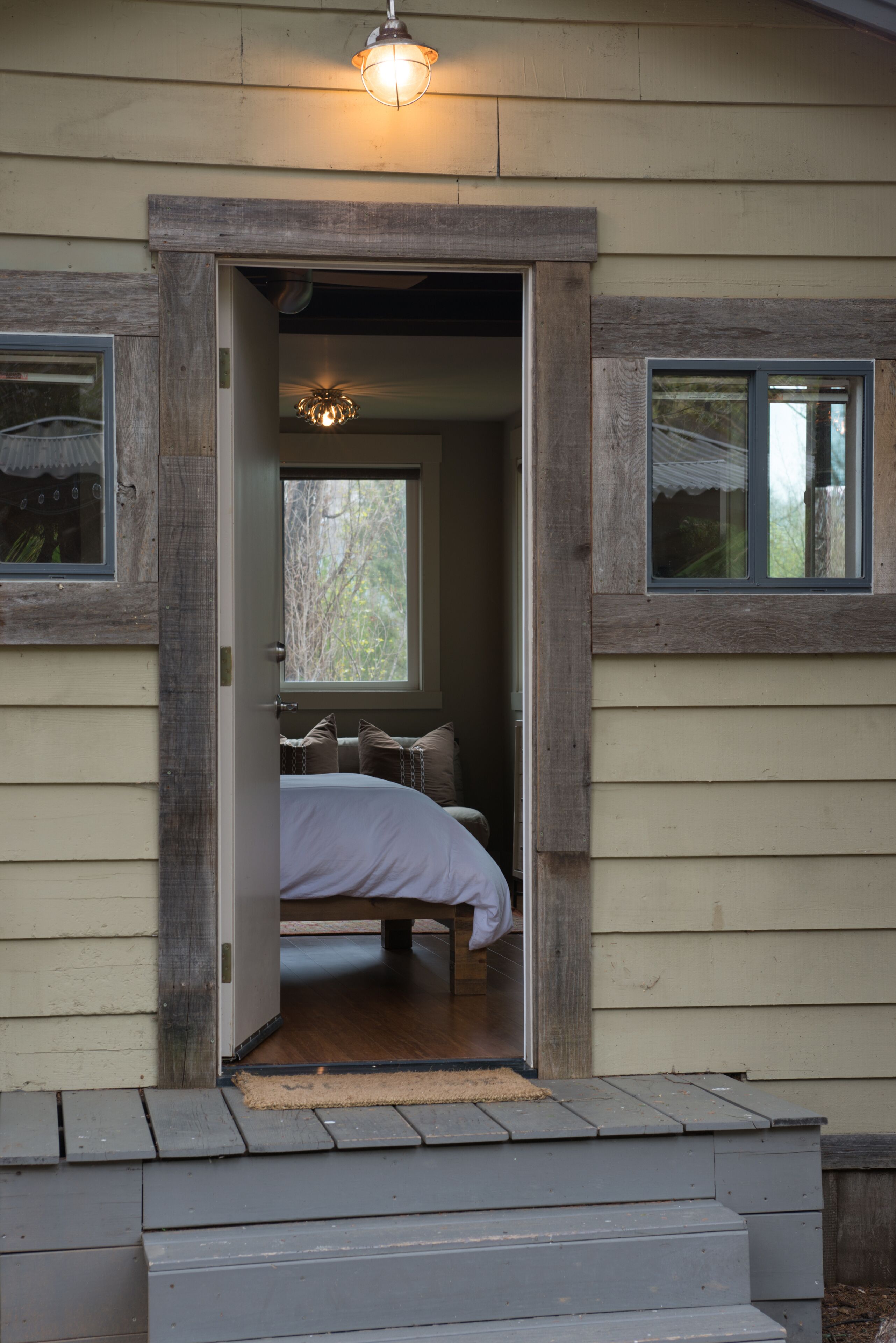 Eine Holztür, die in ein Schlafzimmer mit einem Bett, einem Fenster und einer Leuchte über der Tür führt.