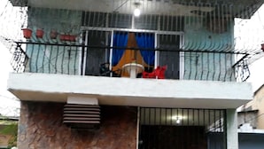 Un edificio de dos pisos con fachada de piedra, un balcón con barandilla de metal y una entrada con rejas.
