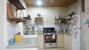 Cocina compacta con estufa, horno y refrigerador, que cuenta con estantes de madera y salpicadero de azulejos.