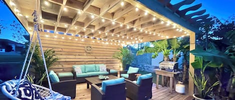 Une terrasse extérieure avec un plancher en bois, un fauteuil suspendu et un ensemble de canapés.