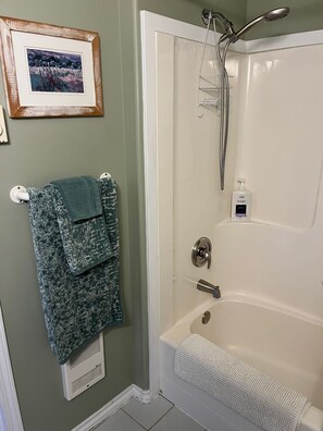 A bathroom with a bathtub, a towel rack with two towels, a framed picture on the wall, and a bottle of Ivory soap. - Delightful Country Cottage with Ocean Outlook (Pender Island)