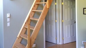 Un escalier en bois dans une pièce aux murs vert clair et au plafond en bois.