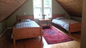 Une petite chambre mansardée avec deux lits en bois, une fenêtre et une petite table avec une lampe.