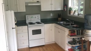 Une cuisine avec des meubles blancs, une cuisinière, un évier et une fenêtre donnant sur un paysage verdoyant.