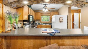 A kitchen with stone walls, wooden cabinets, a central island, and a ceiling fan. - Magic Moments - Pet Friendly Townhome in Innsbruck Golf Community (Helen)