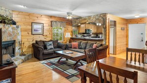 A cozy cabin interior with a stone fireplace, wooden walls, a dining area, and a kitchen with wooden cabinets. - Magic Moments - Pet Friendly Townhome in Innsbruck Golf Community (Helen)