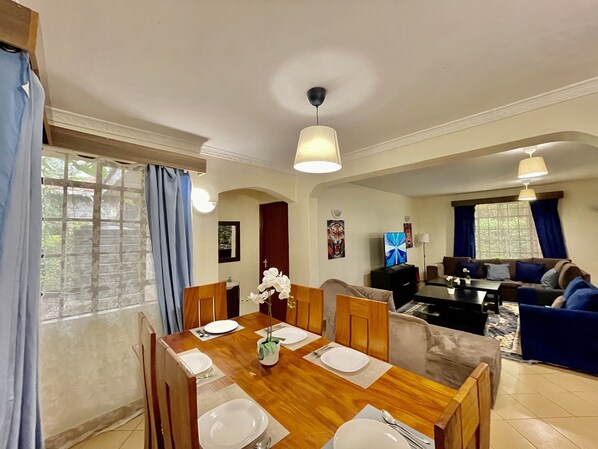 A dining area with a wooden table set for four, a sofa, and a TV in the background.