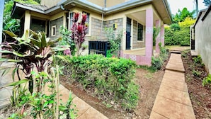 Una casa de dues plantes amb un balcó, envoltada de vegetació i un camí pavimentat.