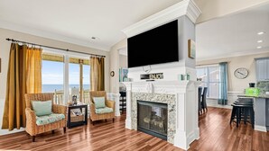 Un salón espacioso con chimenea, dos sillones de mimbre, un televisor de pantalla plana y vista al océano.