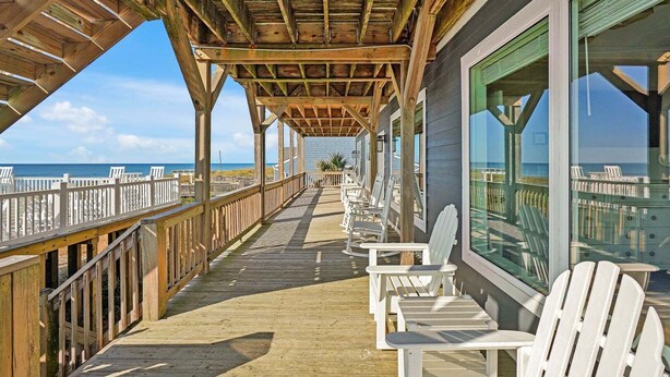 Terraza de madera con sillas blancas y vista al océano.