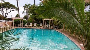 Une piscine dotée de chaises longues et d’un kiosque, entourée de palmiers et d’autres plantes.