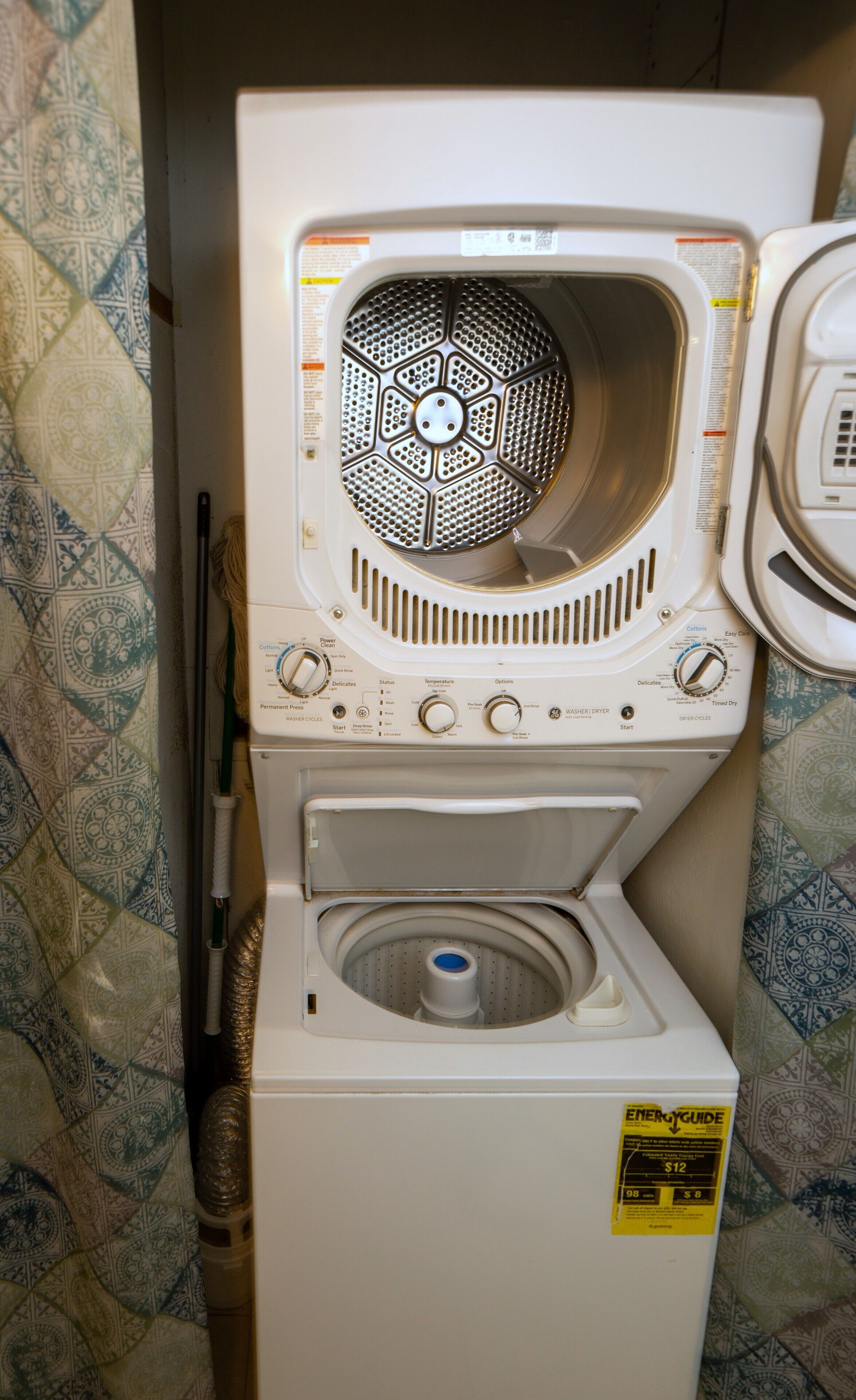 Une machine à laver  à chargement frontal, dotée d’un panneau de commande situé à l’avant, d’un robinet d’arrivée d’eau et d’un compartiment à lessive.