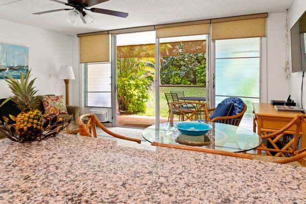 A kitchen with a granite countertop, a dining table with chairs, a ceiling fan, and a view of a garden through large sliding glass doors.