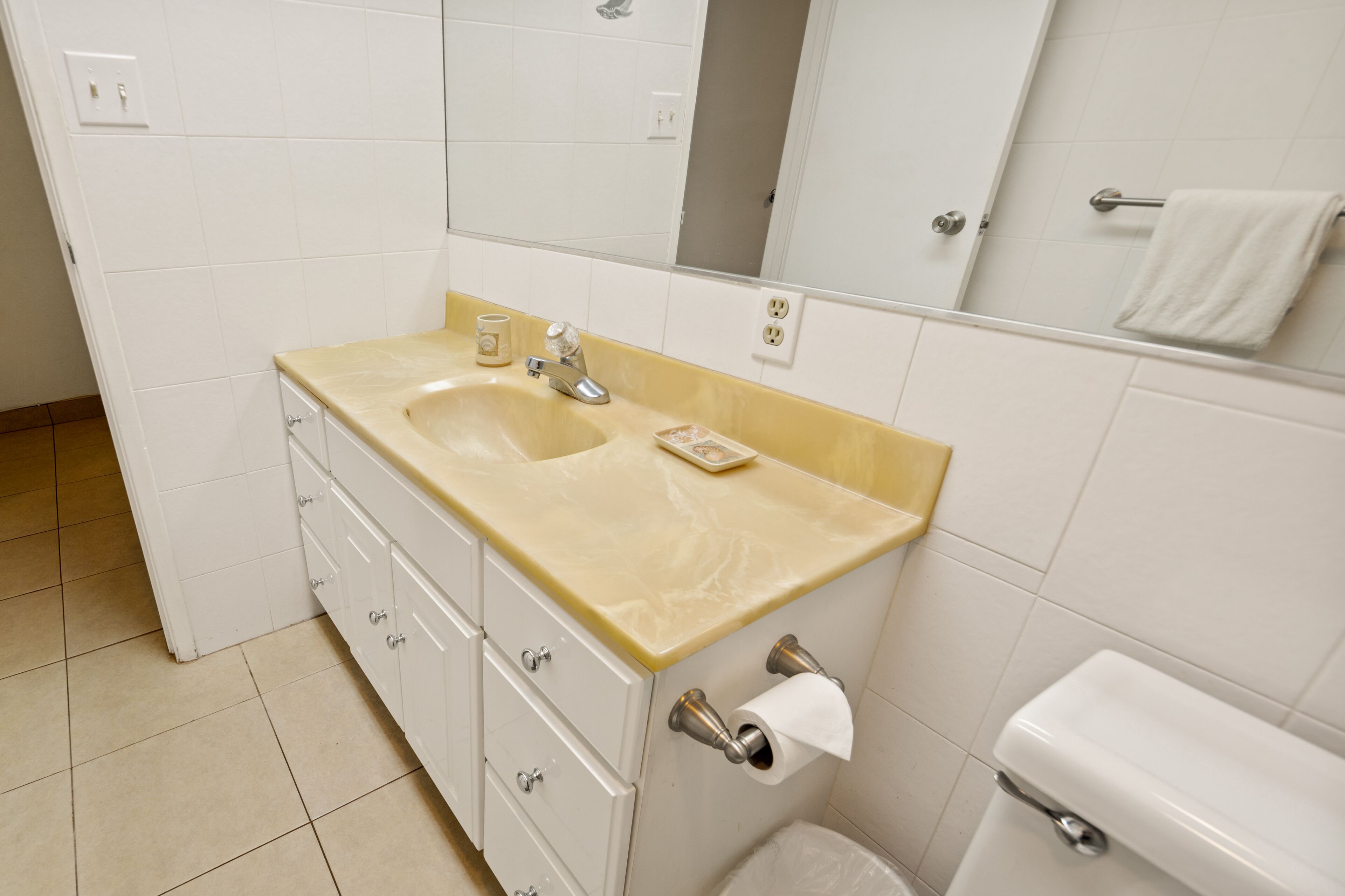 Een badkamer met een beige wastafel, witte kastjes, een spiegel en een toilet.