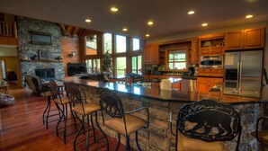 A spacious kitchen with a large island, wooden cabinets, and a stone fireplace.