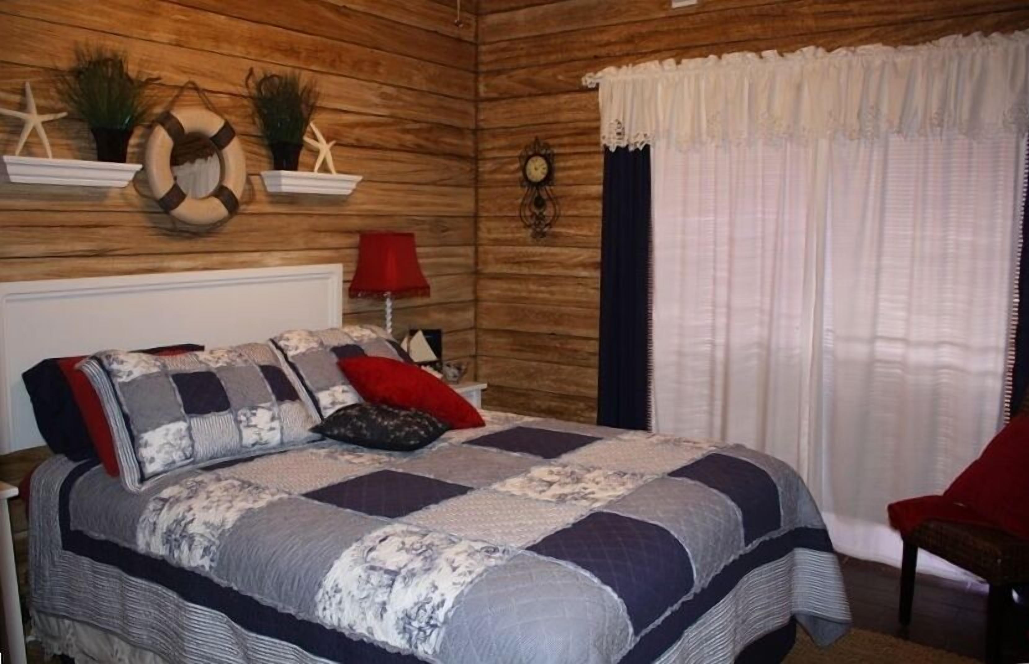 A bedroom with a wooden wall, a bed with a patterned quilt, a red chair, and nautical-themed decor.
