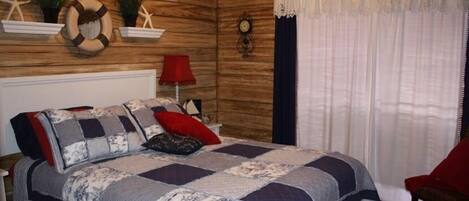 A bedroom with a wooden wall, a bed with a patterned quilt, a red chair, and nautical-themed decor.