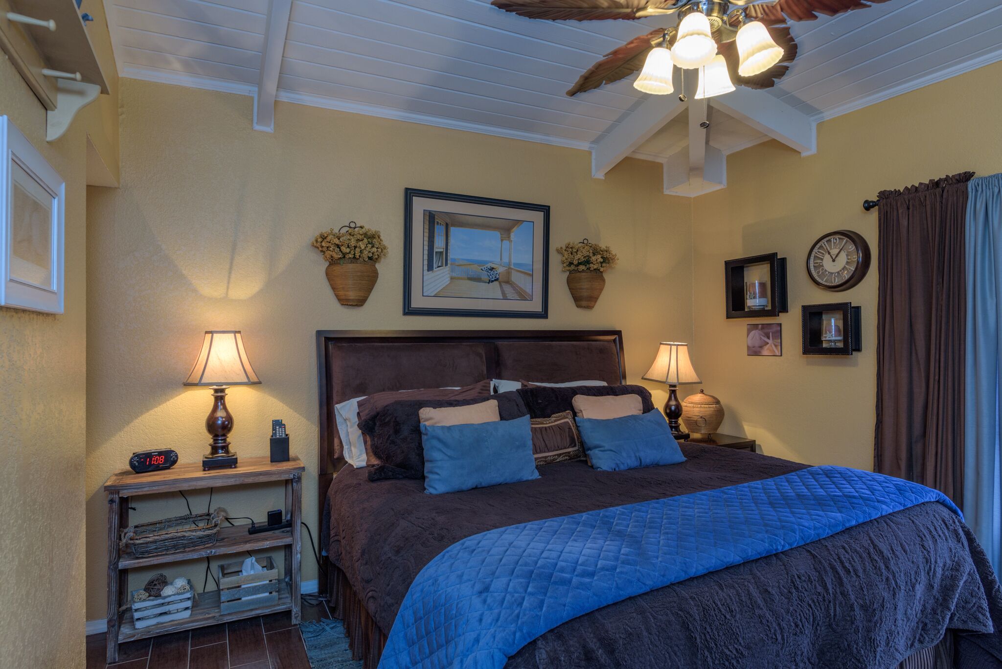 A bedroom with a large bed, two bedside lamps, a clock, and a framed picture on the wall.