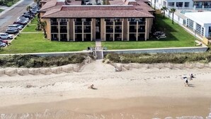 A building with a red roof and large windows, located near a beach with people walking and sitting. - ON THE BEACH  EXCELLENT 5-💎💎💎💎💎 CONDO! Great Rates! 🌴 ⛱️permit: #384879 (South Padre Island)
