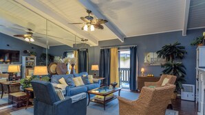 A spacious living room with a blue sofa, a wicker armchair, and a coffee table. There is a ceiling fan, a fireplace, and a large window with curtains. - ON THE BEACH  EXCELLENT 5-💎💎💎💎💎 CONDO! Great Rates! 🌴 ⛱️permit: #384879 (South Padre Island)