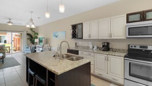 A modern kitchen with a central island, stainless steel appliances, and a dining area visible through an open door. - ⭐Amazing Location-Complex Pool-Balcony and Patio-Corner Unit-2BR Gulf Walk 606⭐ (Destin)