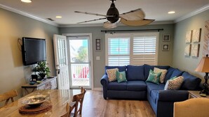 A living room with a dark blue sectional sofa, a wooden dining table with chairs, a ceiling fan, and a television mounted on the wall. - Prime Location 2nd row!!! Beautiful beach views from the deck!!  (Emerald Isle)