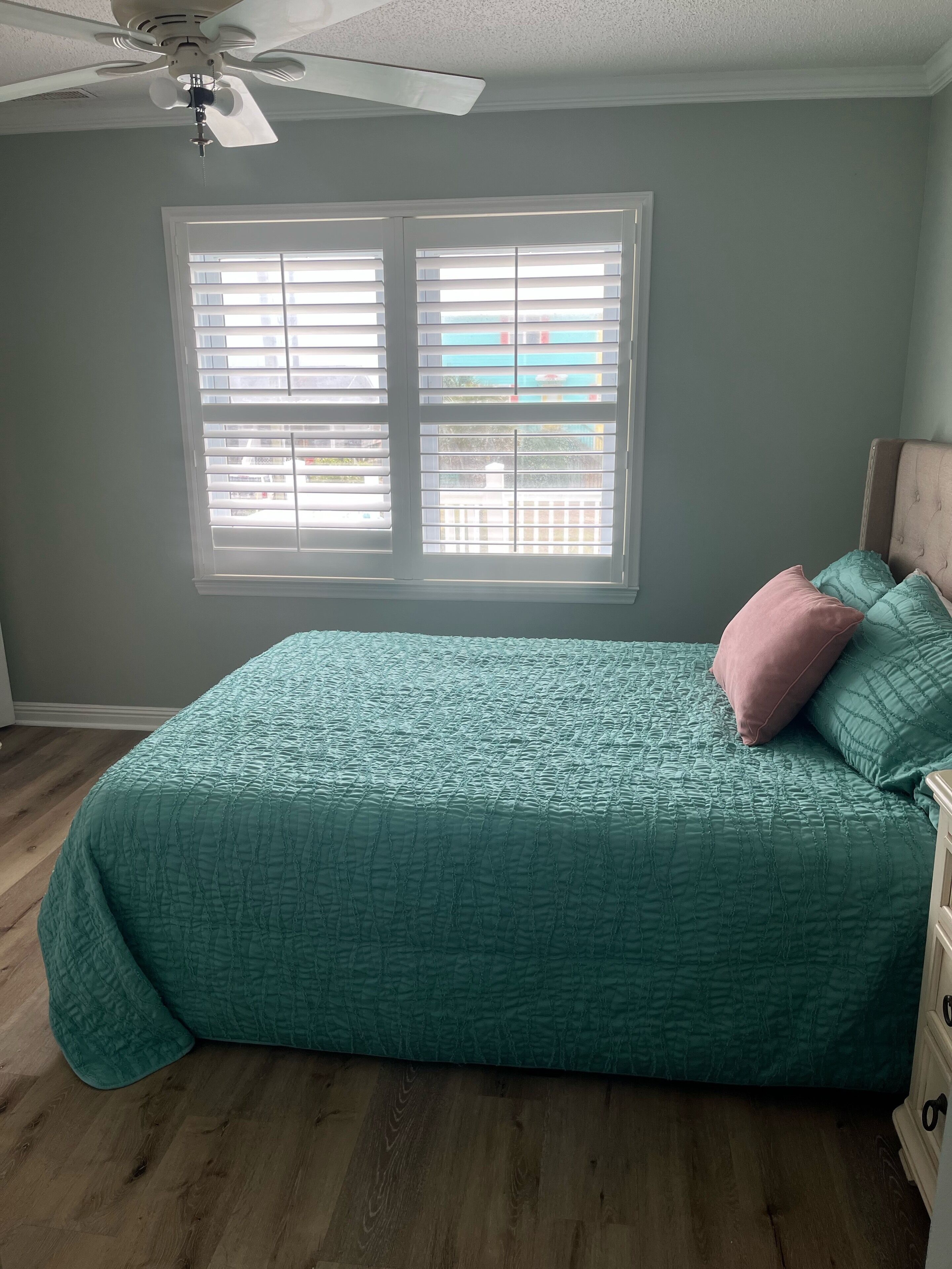Une chambre à coucher avec un lit, un ventilateur de plafond et une fenêtre avec des stores.