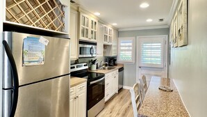 A modern kitchen with stainless steel appliances, white cabinetry, and a wooden floor. - Prime Location 2nd row!!! Beautiful beach views from the deck!!  (Emerald Isle)