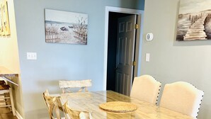 A dining area with a wooden table and chairs, a woven placemat, and artwork on the walls. - Prime Location 2nd row!!! Beautiful beach views from the deck!!  (Emerald Isle)