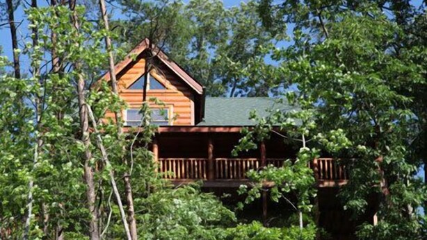 Une cabane en bois dotée d’un balcon, entourée d’arbres.