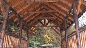 Un pavillon en bois, doté d’une conception simple et ouverte, et offrant une vue sur une zone boisée en arrière-plan.