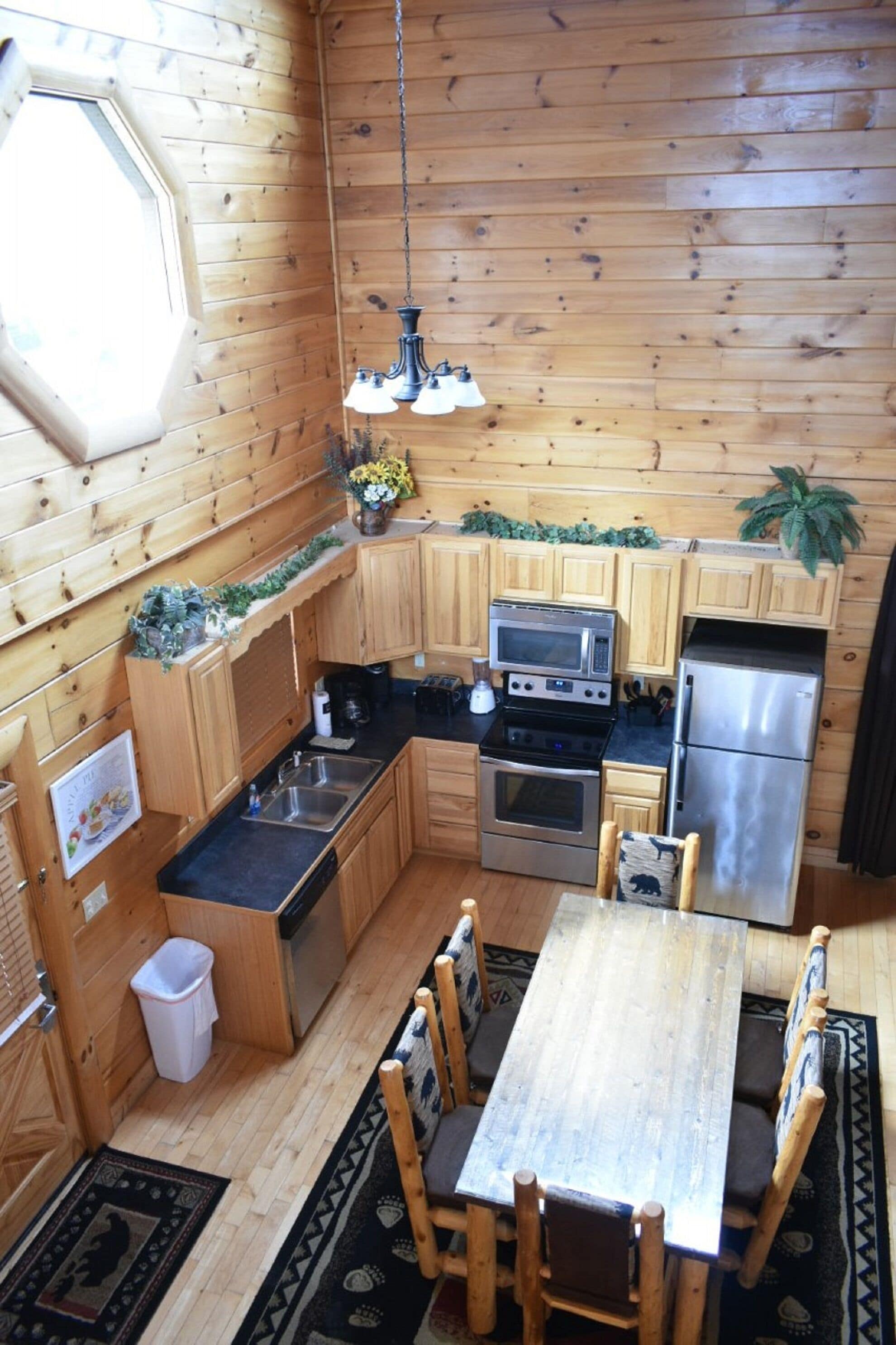 A compact kitchen with wooden cabinetry, a microwave, oven, and refrigerator. There is a dining table with chairs and a hanging light fixture.