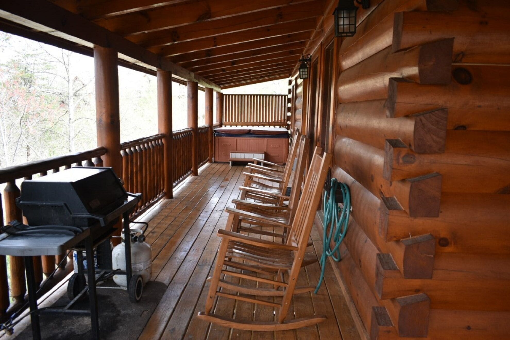 A wooden cabin with a porch, a grill, and several rocking chairs.