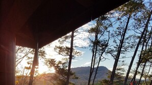 Une vue depuis un espace abrité, doté d’une balustrade en bois, donnant sur une forêt aux couleurs automnales et sur des montagnes lointaines.