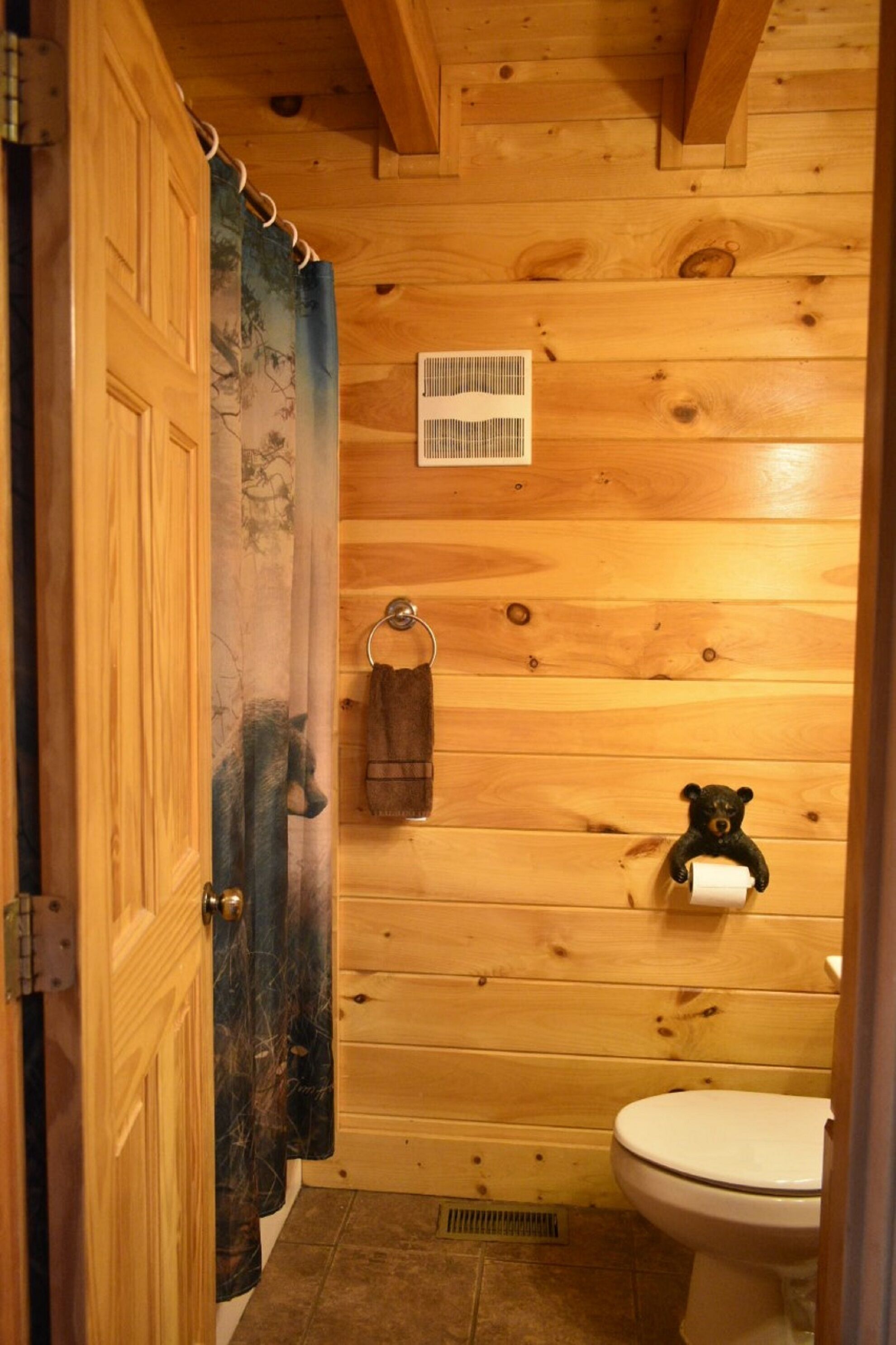 Een badkamer met houten lambrisering, een toilet, een handdoekhouder en ventilatie.
