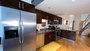 A modern kitchen with stainless steel appliances, dark wooden cabinets, and a yellow rug.