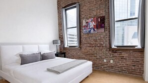 A modern bedroom with a large bed, a brick wall, and large windows.