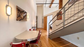 A dining area with a round table and red chairs, a wooden floor, and a staircase with metal railings.